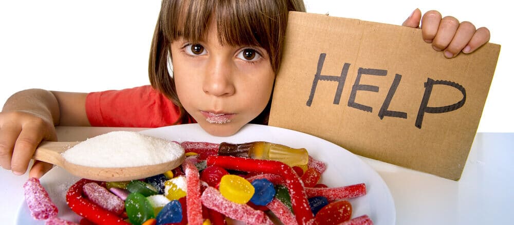 Little girl eating unhealthy and sugary foods while holding up a cardboard sign labelled HELP.