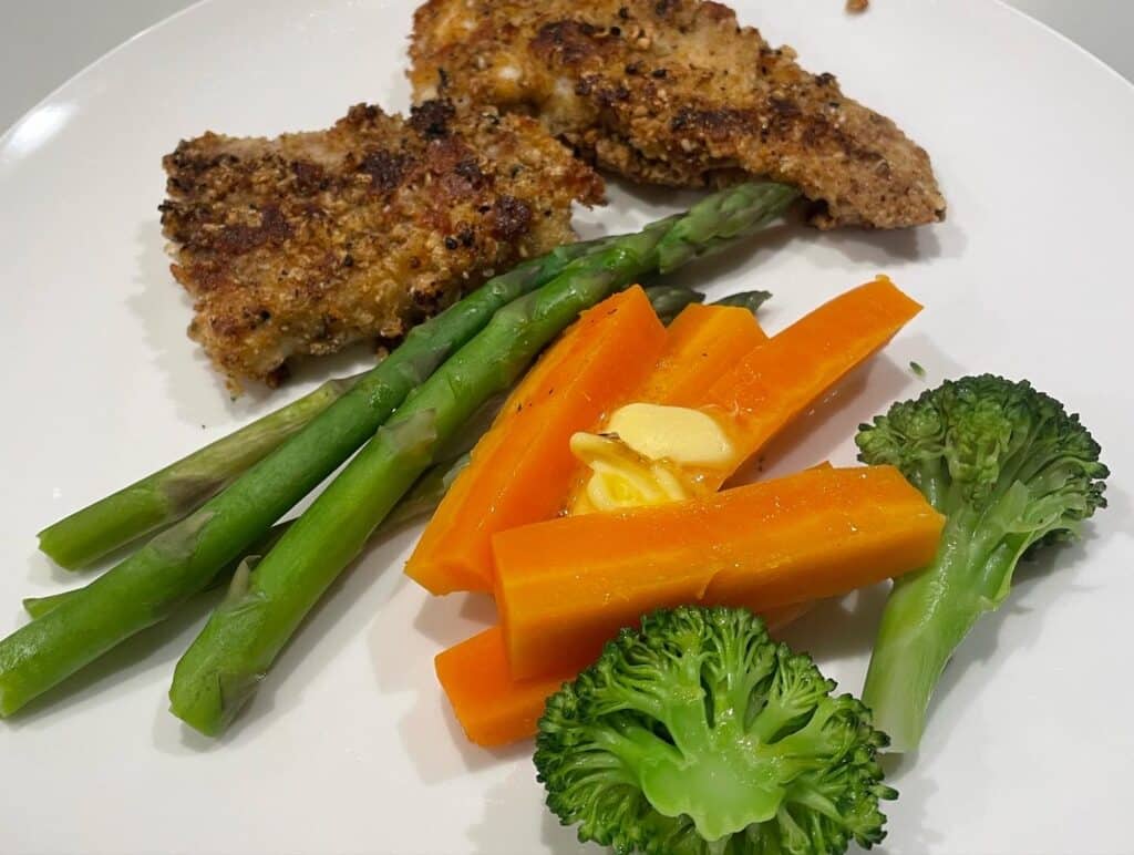 Crumbed fish with asparaguses, carrots, and broccoli on dinner plate.