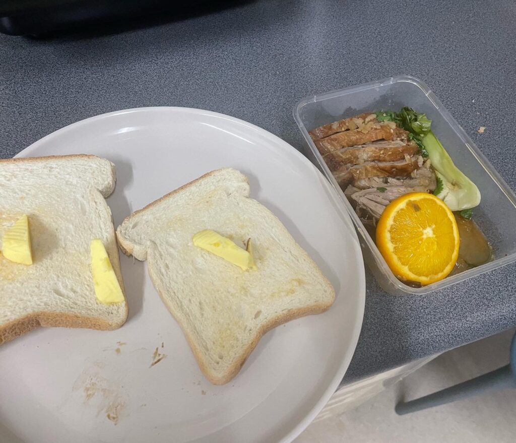 2 slices of toast on plate next to a plastic container filled with cooked duck in orange sauce.