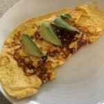Omelet on plate with 3 avocados on top.