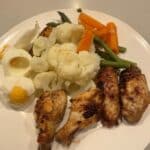 Chicken wings, cauliflower, asparagus, carrots on dinner plate.