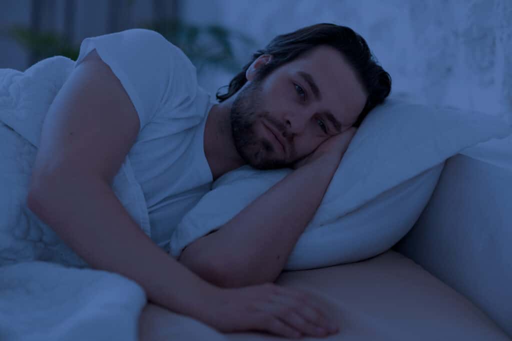 Man laying awake on his bed struggling with insomnia.