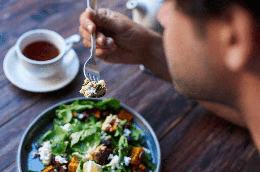 Man eating a healthy salad from a bowl with a cup of tea next to him.