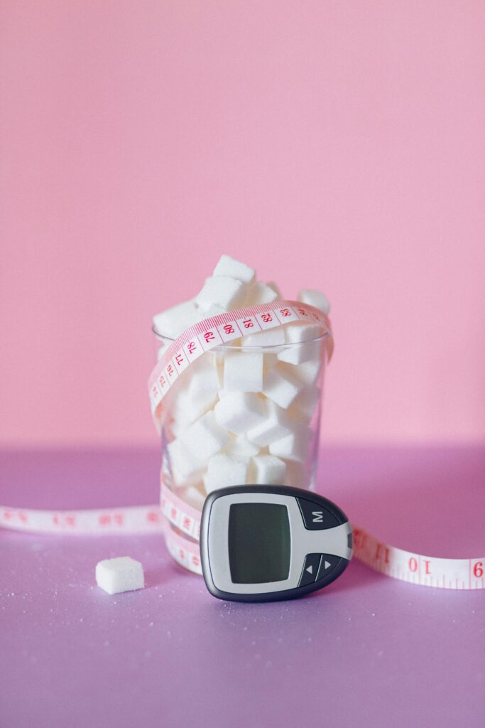 Sugar in glass cup with measuring tape wrapped around it and a diabetes test sitting next to the cup.