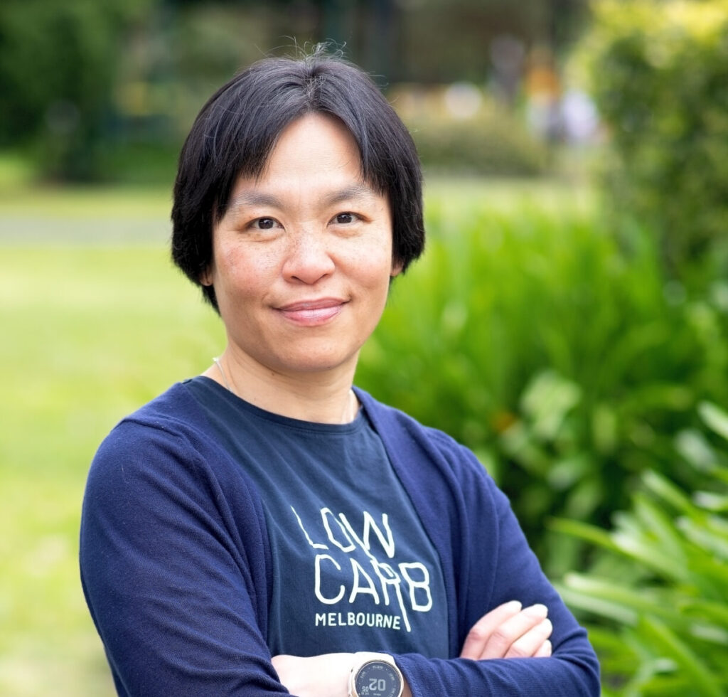 Dr. Avi Charlton, a low carb GP standing in front of bushes and smiling with her arms crossed.