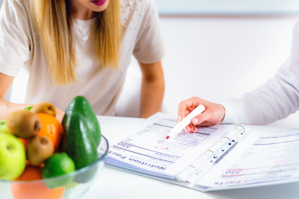 Metabolic clinic doctor showing a patient her diet plan on paper with a bowl of healthy fruits next to them.