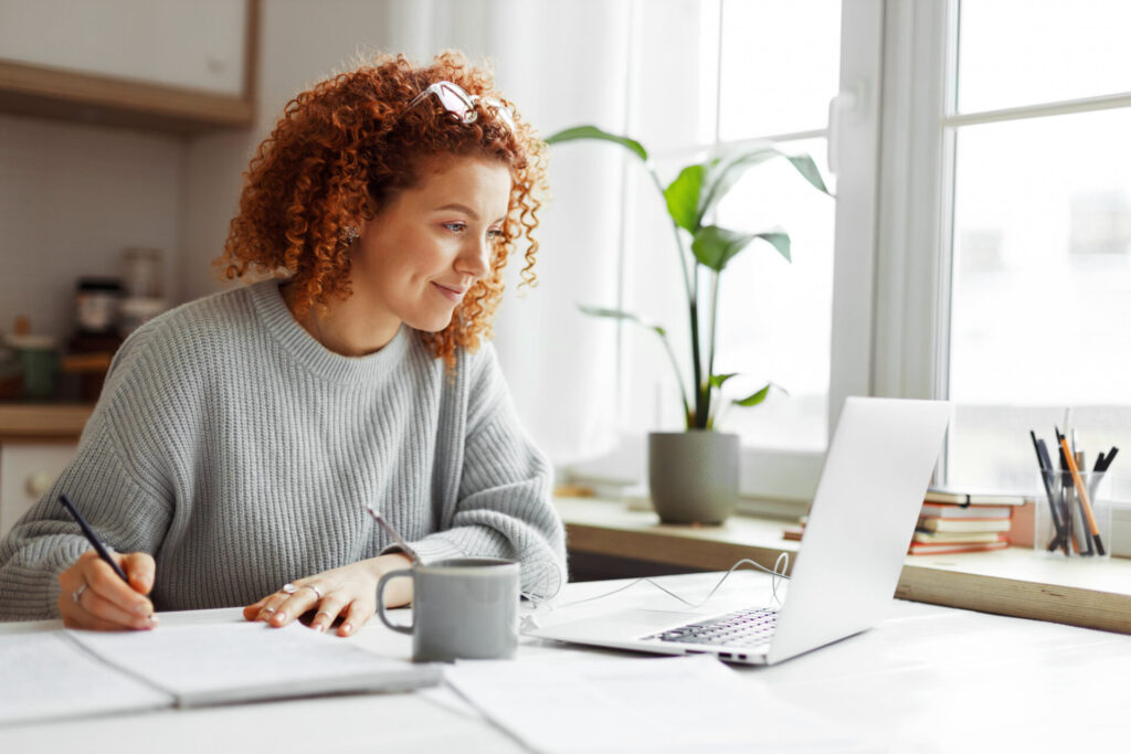 Woman taking notes in notebook while on video call with her online weight loss doctor.